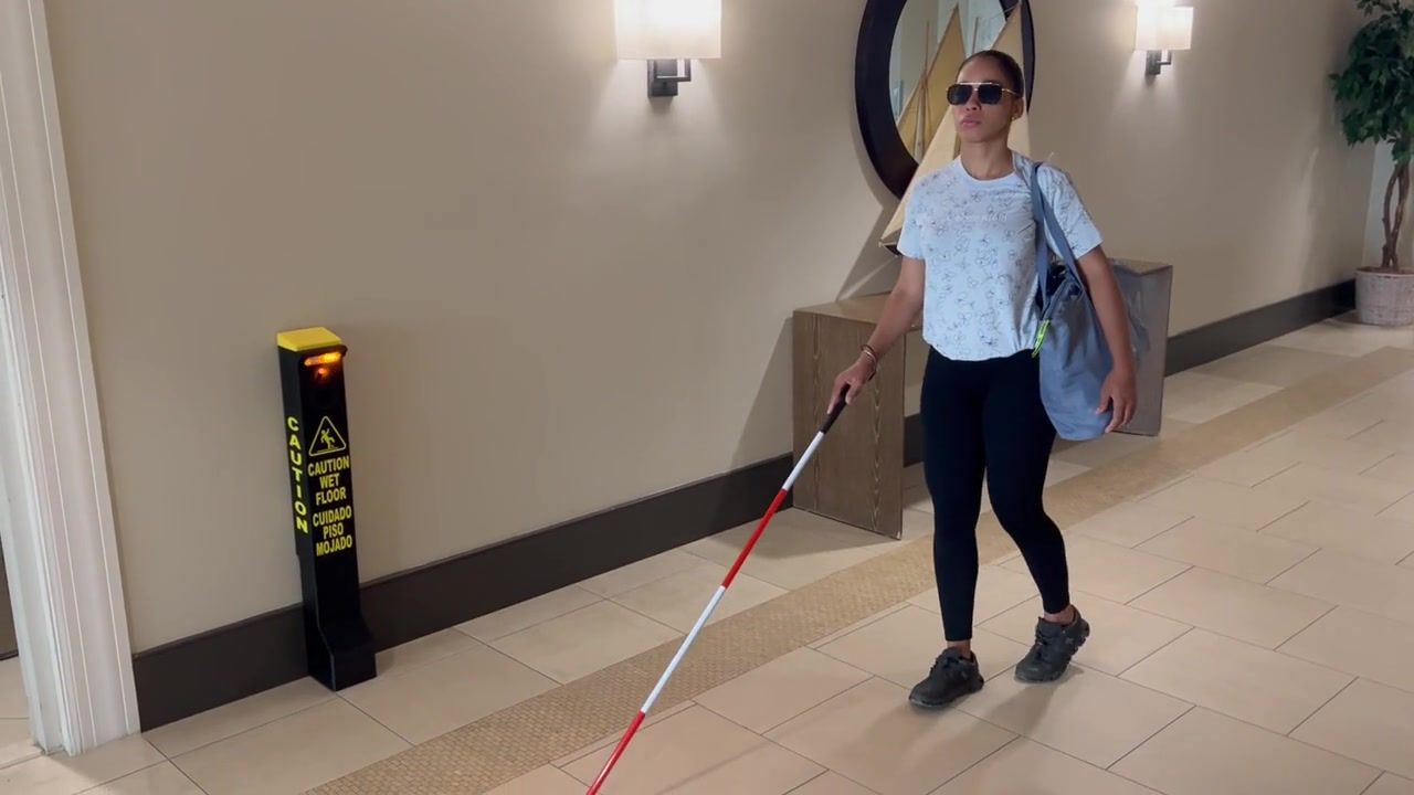 Woman with a white cane walking past the Safety Illuminator Wall Mount Model in a hallway